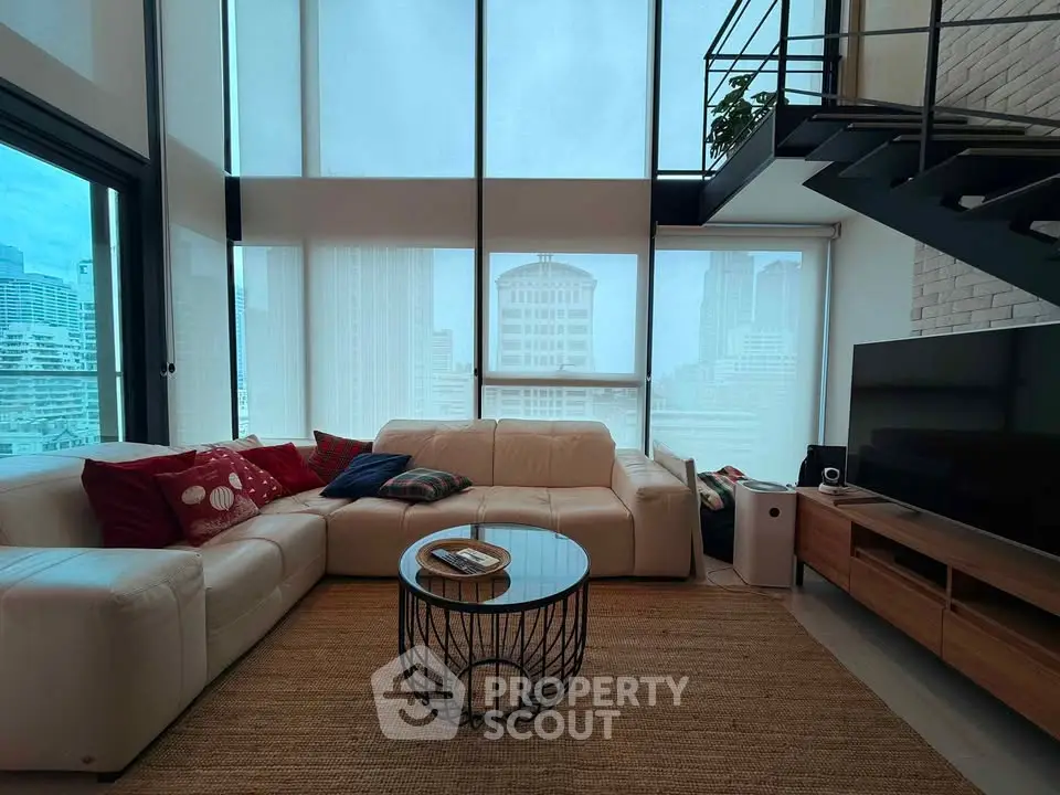 Spacious modern living room with large windows and city view, featuring a cozy sectional sofa and stylish decor.