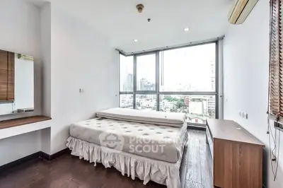 Bright bedroom with large windows and city view, featuring a comfortable bed and modern decor.