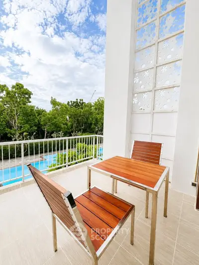 Charming balcony with pool view, featuring modern wooden furniture and lush greenery, perfect for relaxation.
