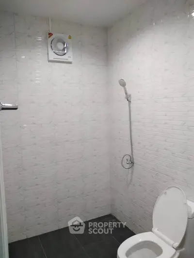 Modern bathroom with tiled walls and showerhead, featuring a sleek toilet design.