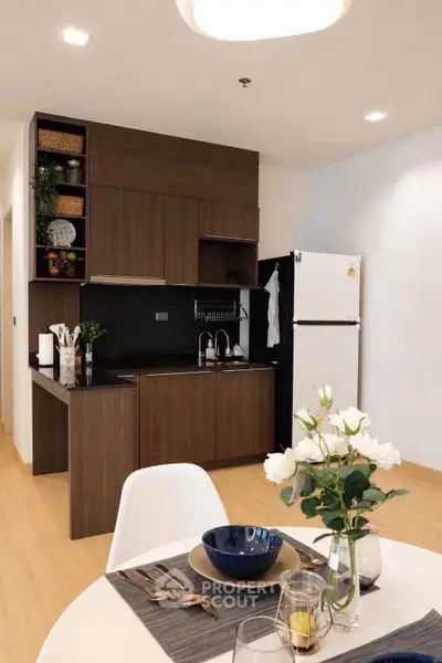 Modern kitchen with dark wood cabinets and white fridge, open layout with dining area, stylish and functional.