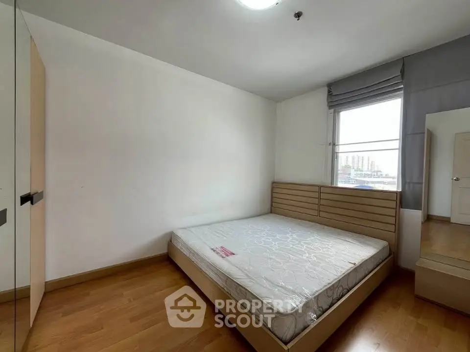 Spacious bedroom with large window and wooden flooring in modern apartment.