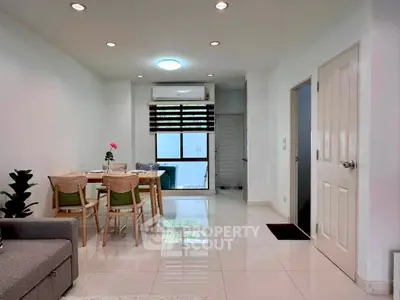 Modern living room with dining area and natural light, featuring sleek furniture and minimalist decor.