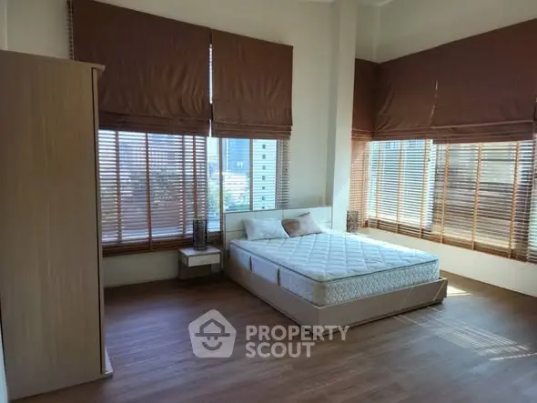 Spacious bedroom with large windows and wooden flooring in modern apartment.