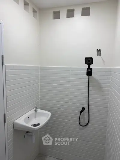 Minimalist bathroom with white tiles and wall-mounted sink and showerhead.