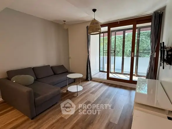 Modern living room with large windows and balcony access, featuring stylish decor and wooden flooring.