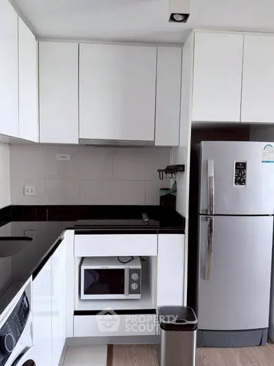 Modern kitchen with sleek white cabinets, stainless steel fridge, and built-in microwave.