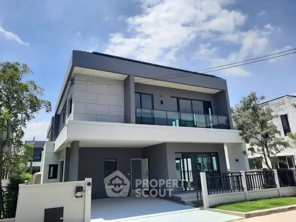 Modern two-story house with sleek design and spacious balcony under clear blue sky.