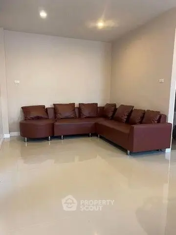 Spacious living room with modern brown leather sectional sofa and polished tile flooring.