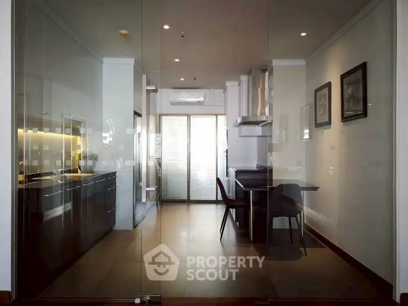 Modern kitchen with sleek black cabinets and glass doors, featuring a dining area and natural light.