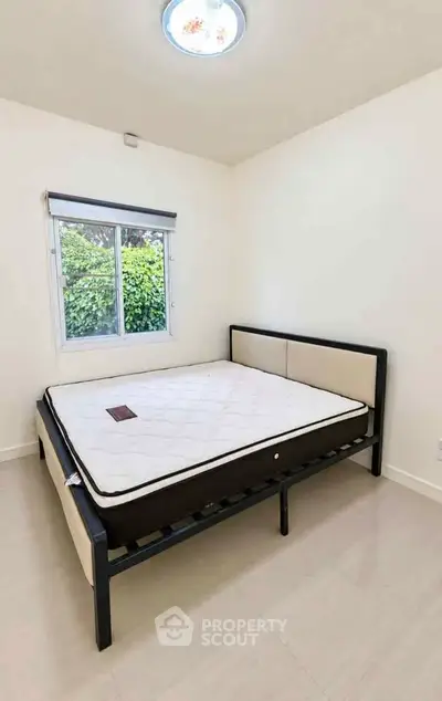 Spacious bedroom with modern bed frame and large window offering garden view.