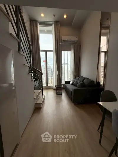 Modern loft apartment with high ceilings and city view, featuring a cozy living area and stylish staircase.