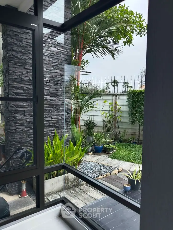 Modern home with lush garden view through large glass windows, featuring sleek stone wall accents.