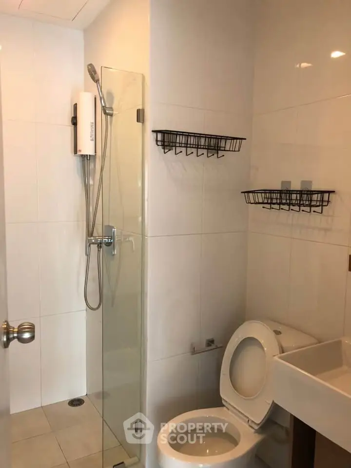Modern bathroom with glass shower, white tiles, and wall-mounted storage racks.