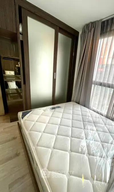 Modern bedroom with large window and sliding wardrobe doors, featuring a comfortable mattress.