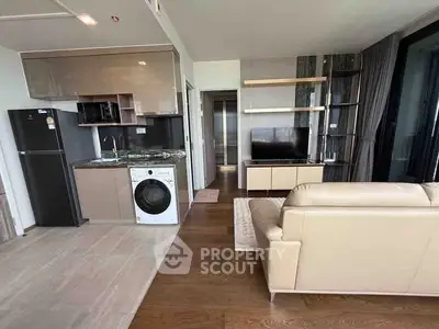 Modern living room with open kitchen, featuring washing machine and sleek furniture.