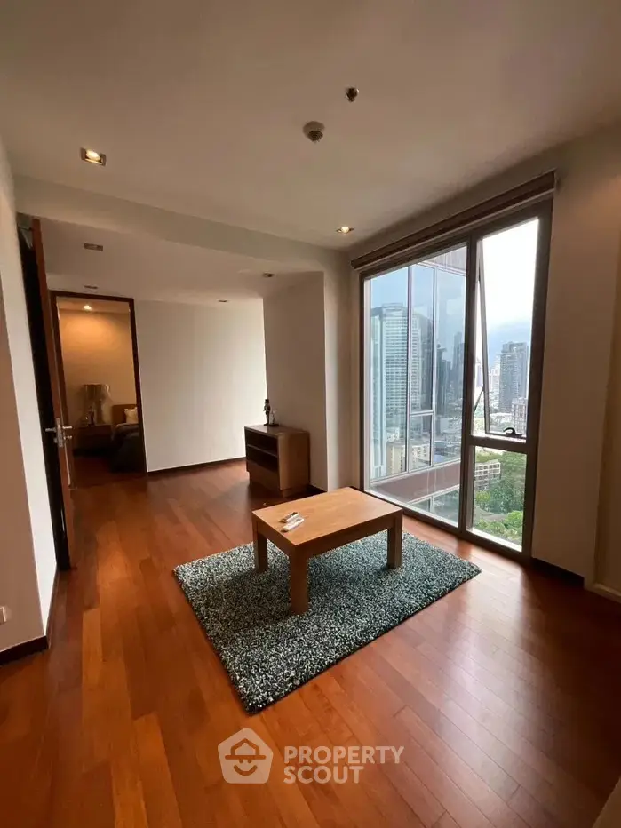 Spacious living room with wooden flooring and stunning city view from large windows.