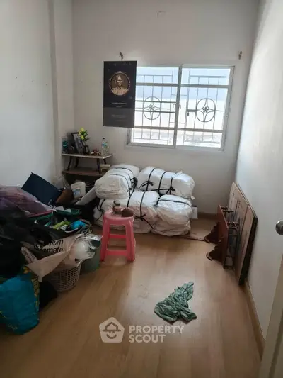 Compact storage room with window and wooden floor, ideal for organizing household items.