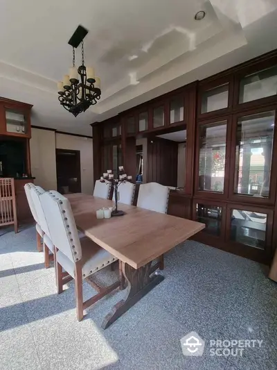 Elegant dining area with wooden table and chairs, featuring large windows and stylish chandelier.