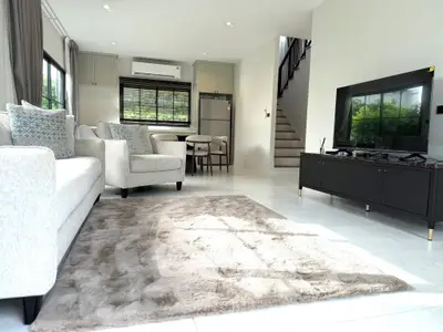 Spacious modern living room with plush rug and stylish furniture, featuring a sleek TV setup and large windows.