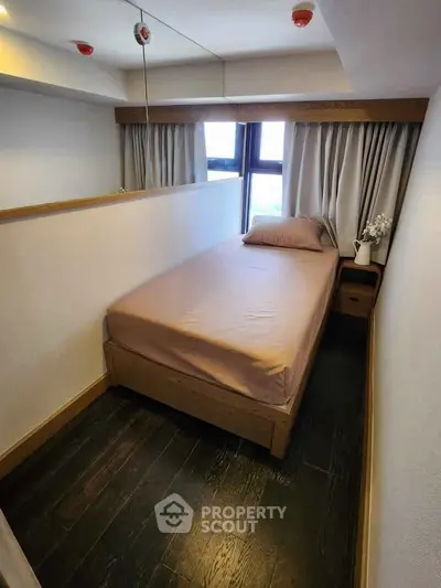 Cozy bedroom with single bed and large window, featuring elegant curtains and a small bedside table.