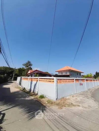 Charming suburban house with red roof and surrounding wall under clear blue sky.