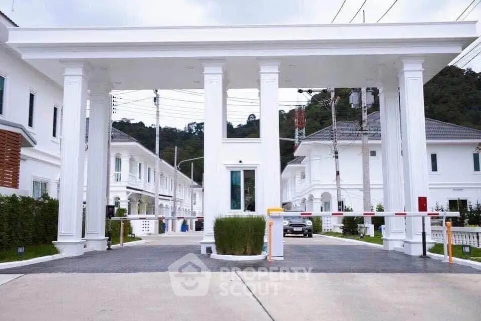 Elegant gated entrance of a luxury residential community with white columns and lush greenery.