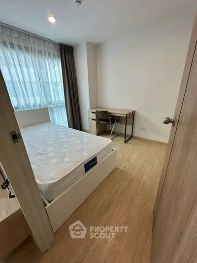 Modern bedroom with wooden flooring, large window, and study desk in a cozy apartment.