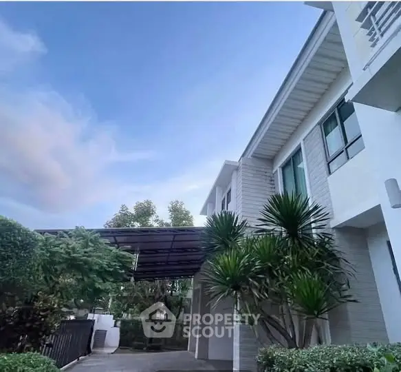 Modern white building exterior with lush greenery and clear blue sky.