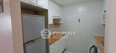 Compact kitchen with white cabinets and wooden countertops, featuring a fridge and washing machine.