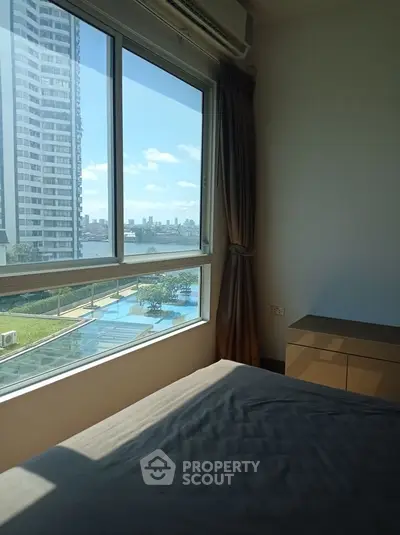 Bright bedroom with stunning river view and modern high-rise building nearby.