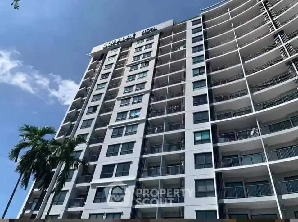 Modern high-rise building with spacious balconies and palm trees under a clear blue sky.