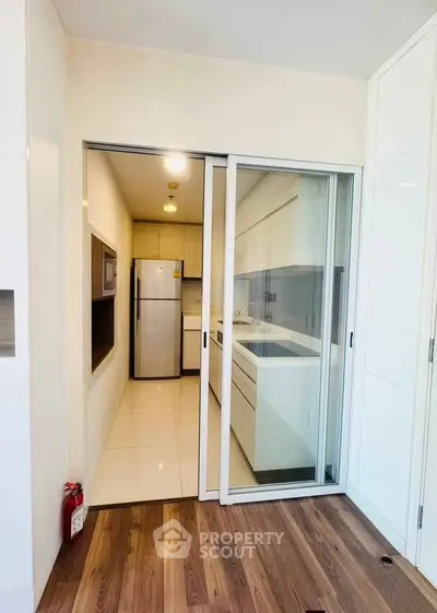 Modern kitchen with sleek design and closed layout featuring built-in appliances and wooden flooring.