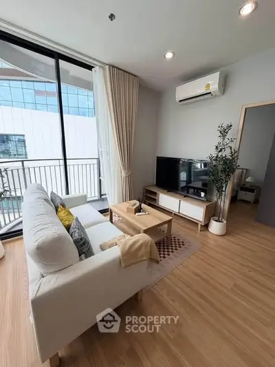 Modern living room with large windows and balcony view, featuring cozy sofa and sleek TV setup.