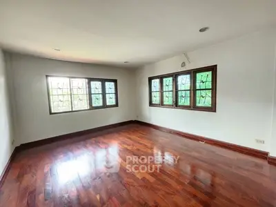 Spacious empty room with polished wooden floors and large windows offering natural light.