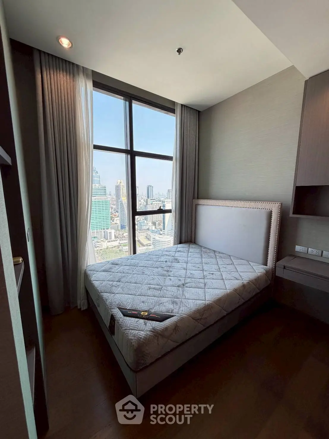 Modern bedroom with city view, featuring large window and stylish decor in a high-rise apartment.