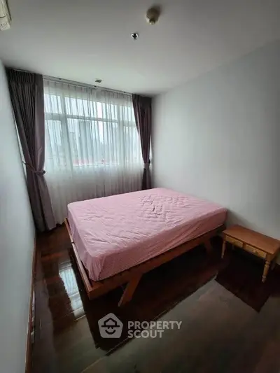 Spacious bedroom with large window and wooden flooring, perfect for cozy living.