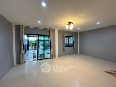 Spacious living room with modern lighting and large windows opening to a patio.