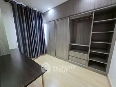 Spacious modern bedroom with built-in wooden wardrobe and elegant curtains.