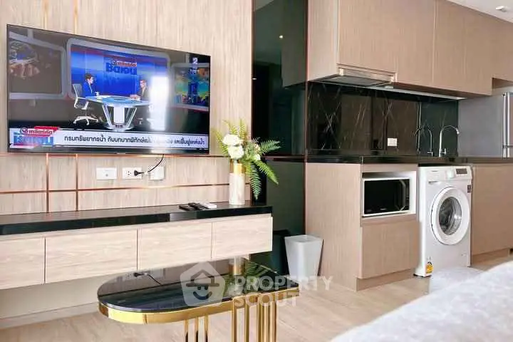 Modern living room with sleek kitchen and built-in appliances, featuring a wall-mounted TV.