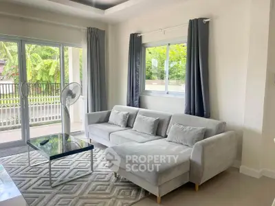 Modern living room with stylish gray sofa and large windows overlooking lush greenery.
