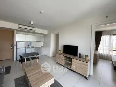 Modern open-plan living room with kitchen and dining area, featuring sleek furniture and natural light.
