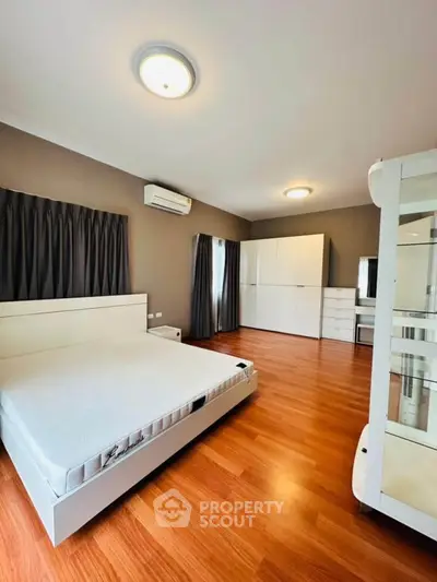 Spacious modern bedroom with wooden flooring and sleek white furniture