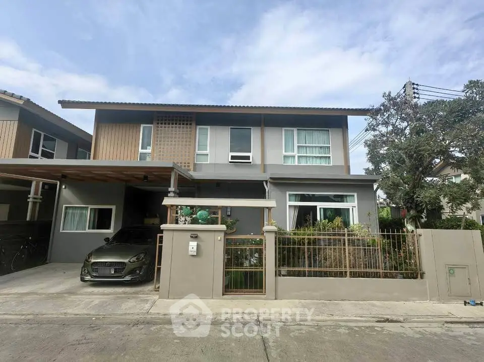 Modern two-story house with carport and lush garden in suburban neighborhood.