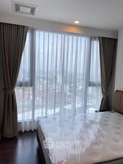 Bright bedroom with large window offering stunning city views, featuring elegant curtains and a comfortable bed.