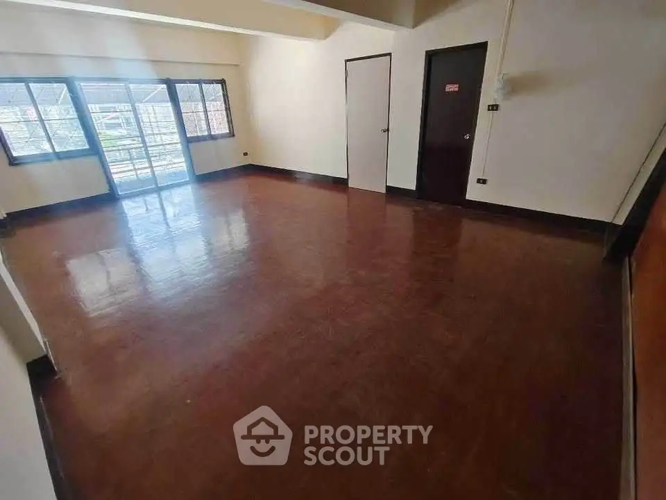 Spacious empty room with polished wooden floors and large windows.