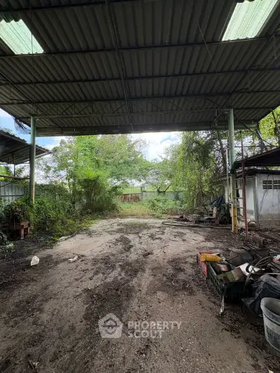 Spacious outdoor area with metal roof and lush greenery, ideal for storage or workshop use.