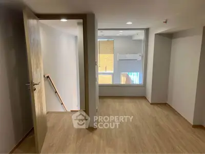 Spacious room with wooden flooring and large window, ideal for versatile use in modern home.