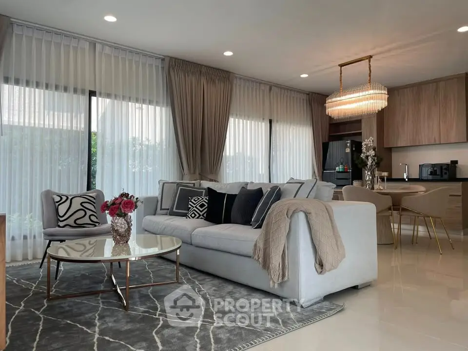 Luxurious modern living room with elegant decor and open kitchen layout, featuring a chic chandelier and cozy seating area.