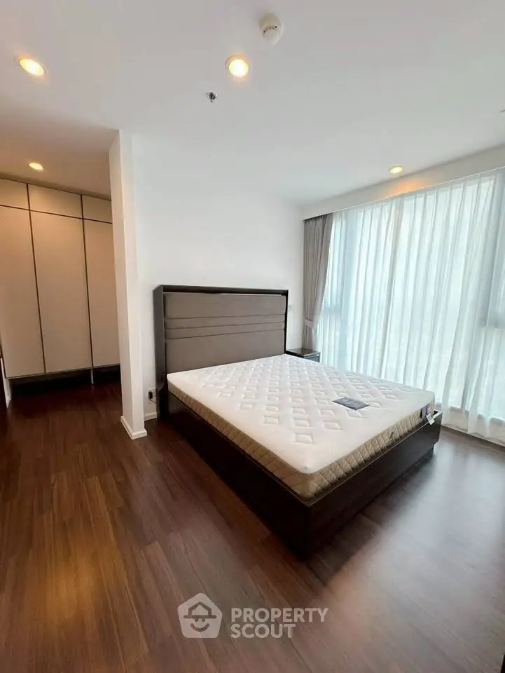Spacious bedroom with large windows and wooden flooring in modern apartment